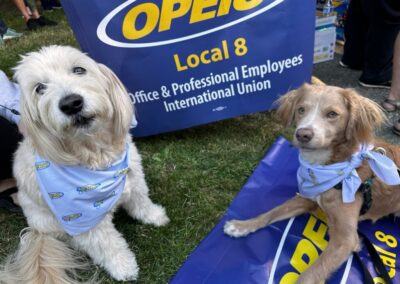 Two dogs pose in front of an OPEIU Local 8 banner while wearing bandanas